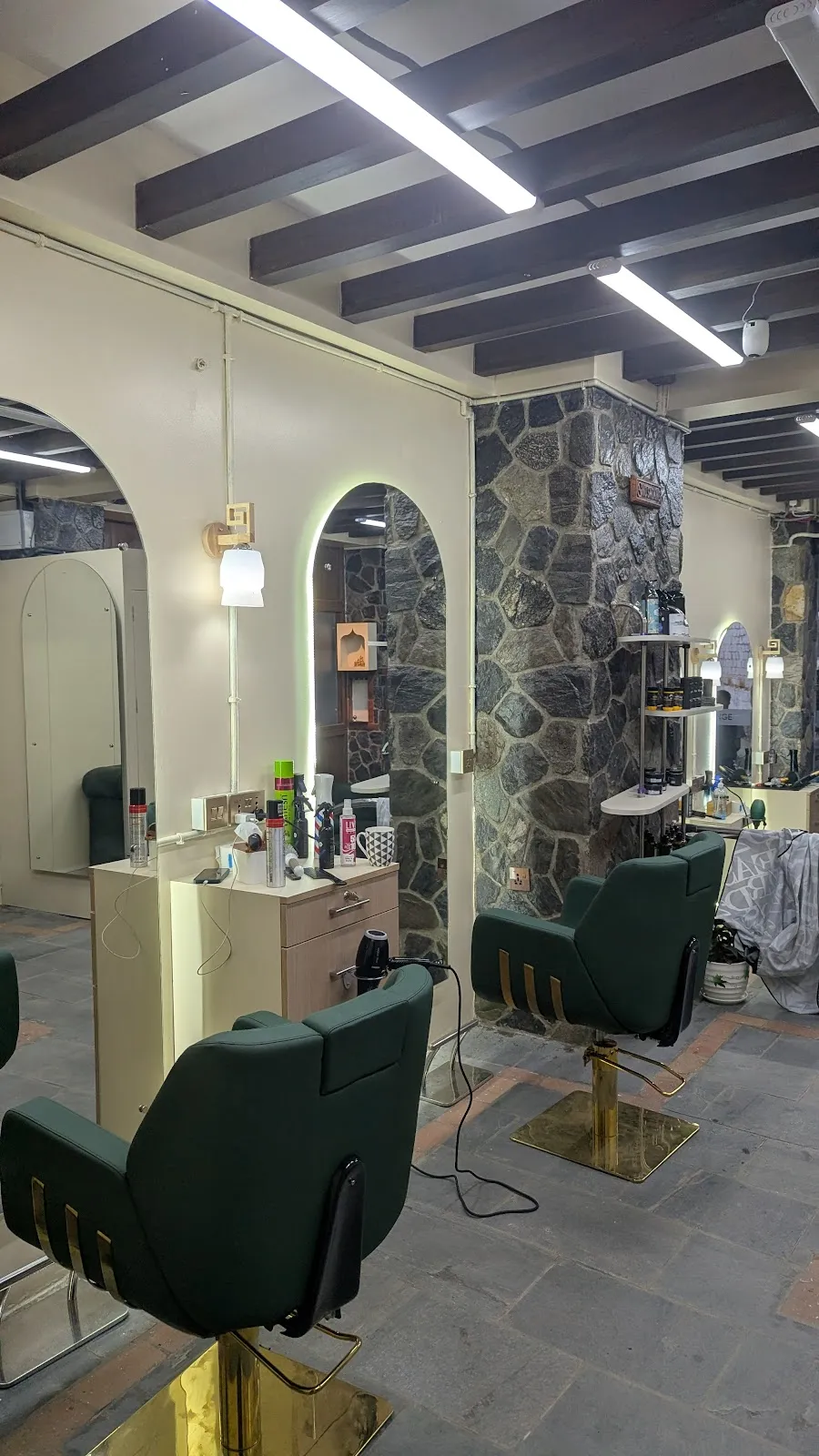 The interior of Ryam's Barber & Beauty Lounge — forest green leather chairs on brass bases, arched mirrors and a rough stone feature wall
