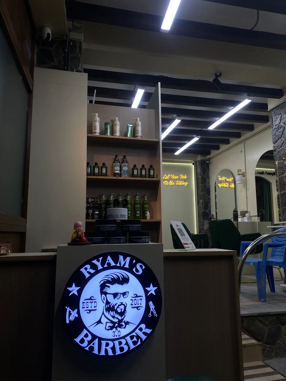 The Ryam's Barber illuminated logo at the front desk, with hair-care products on the shelves behind